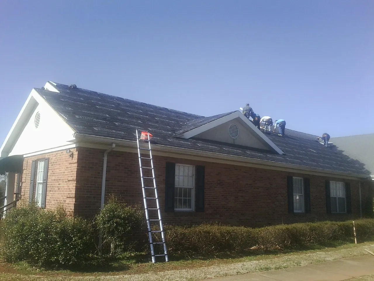 Crew tearing shingles off a brick ranch roof with a ladder set — Metal Roof Repair work by our crew in Lisbon